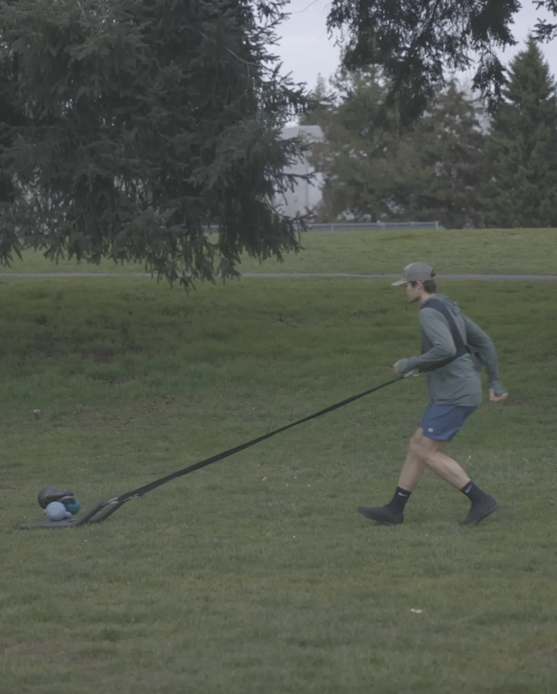 Connor pulling a weighted sled loaded with kettlebells across a park field using a shoulder harness