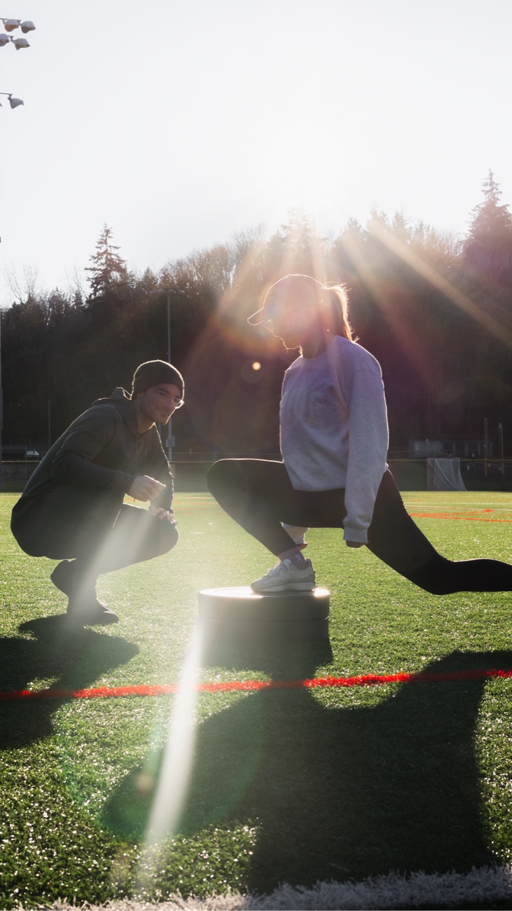 Connor coaching a client through weighted step-ups on a turf field at sunset