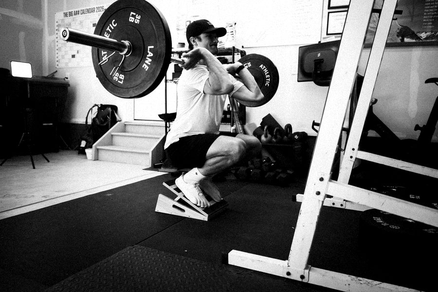 Connor front squatting a barbell on a slant board in his garage gym